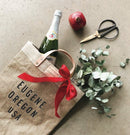 Personalized Apolis Market Bag printed EUGENE OREGON USA, styled with champagne, pomegranate and eucalyptus for holiday gifting